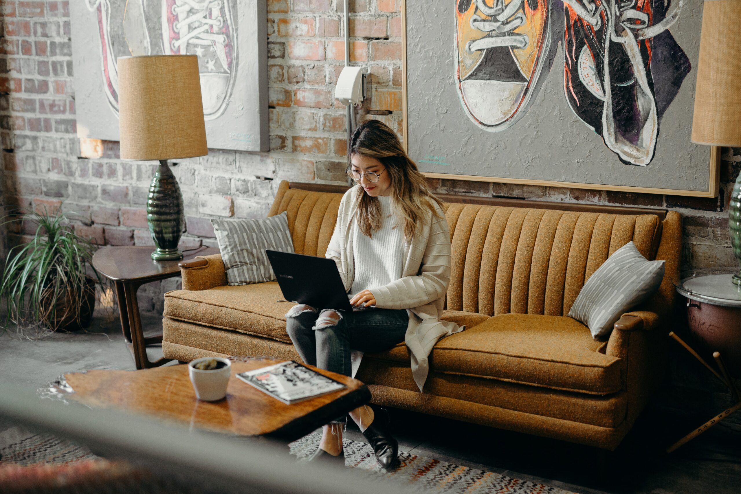 asian woman sitting on sofa working on a laptop in a trendy looking workspace.